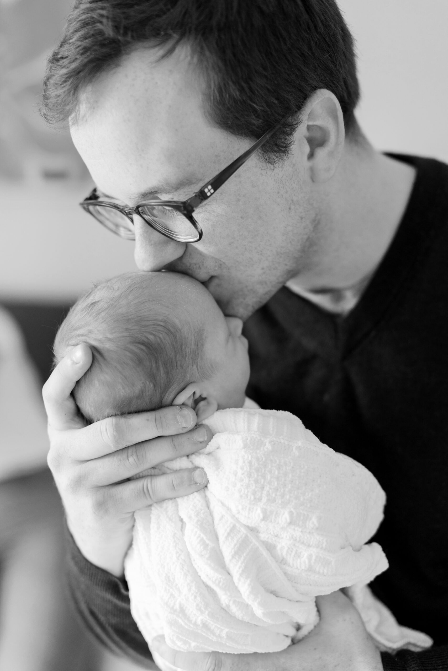 black and white photo of dad kissing baby during newborn photos