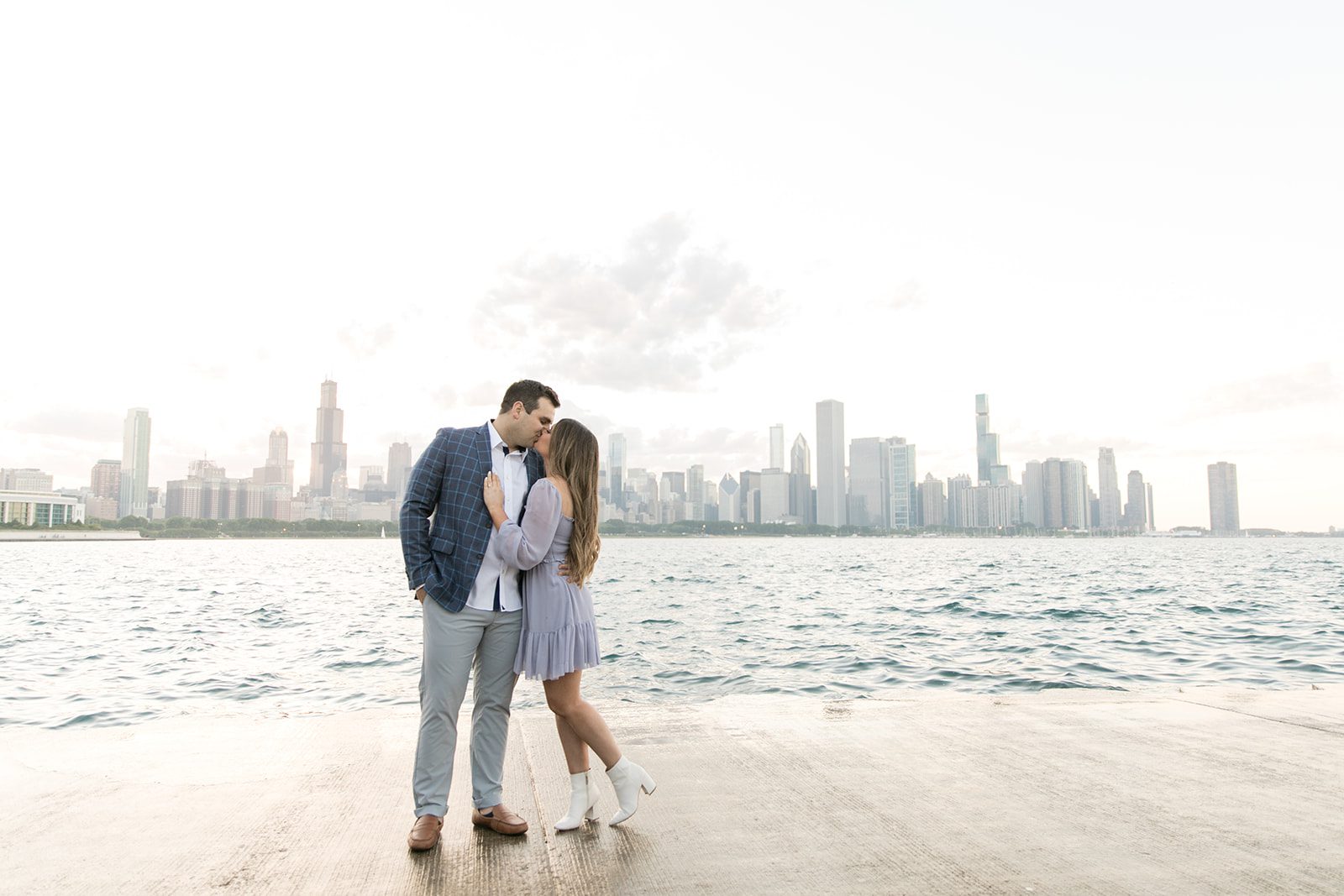 man and woman kiss with the chicago skyline behind them during downtown Chicago engagement photoshoot