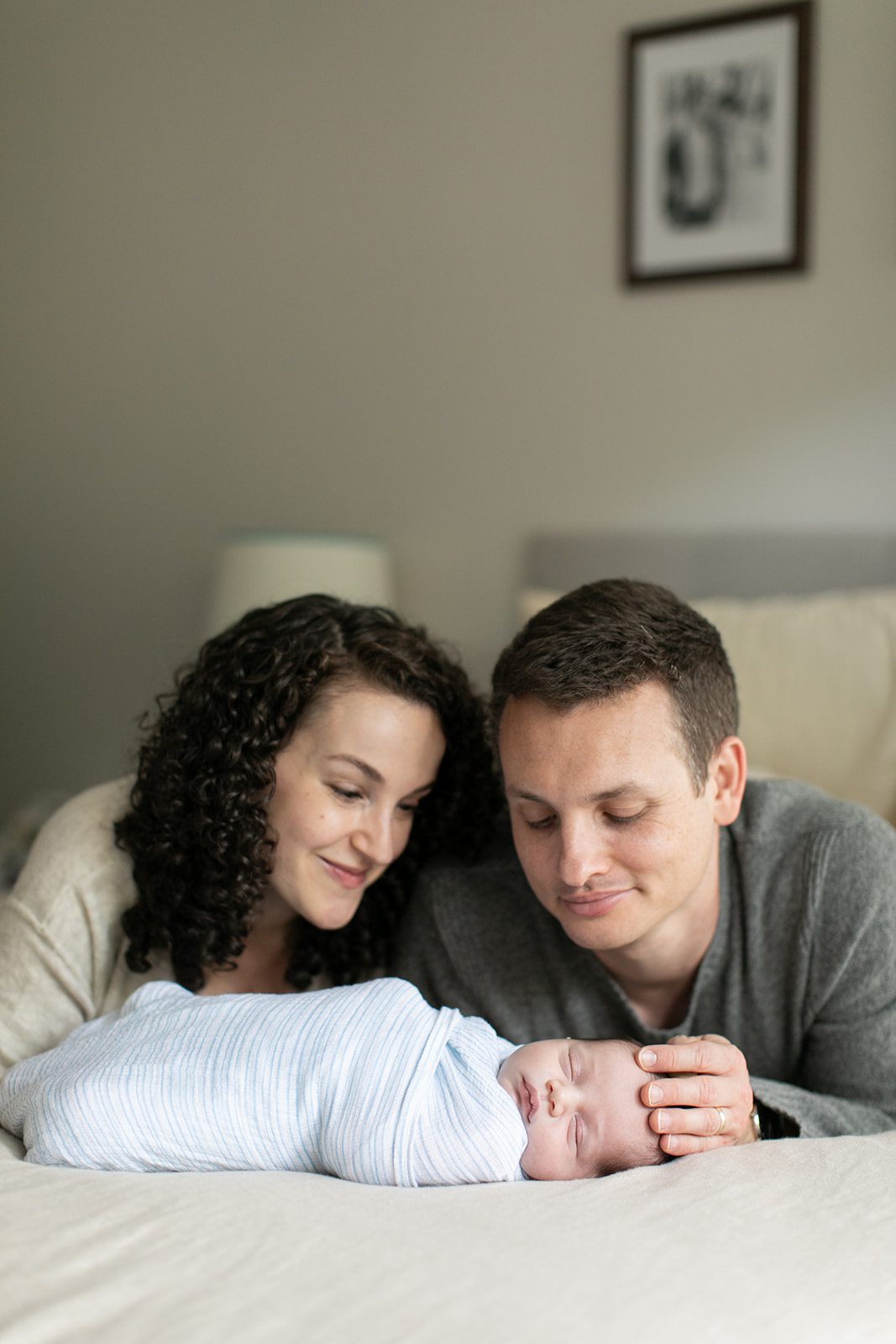 man and woman lay on stomachs on the bed and admire their newborn baby