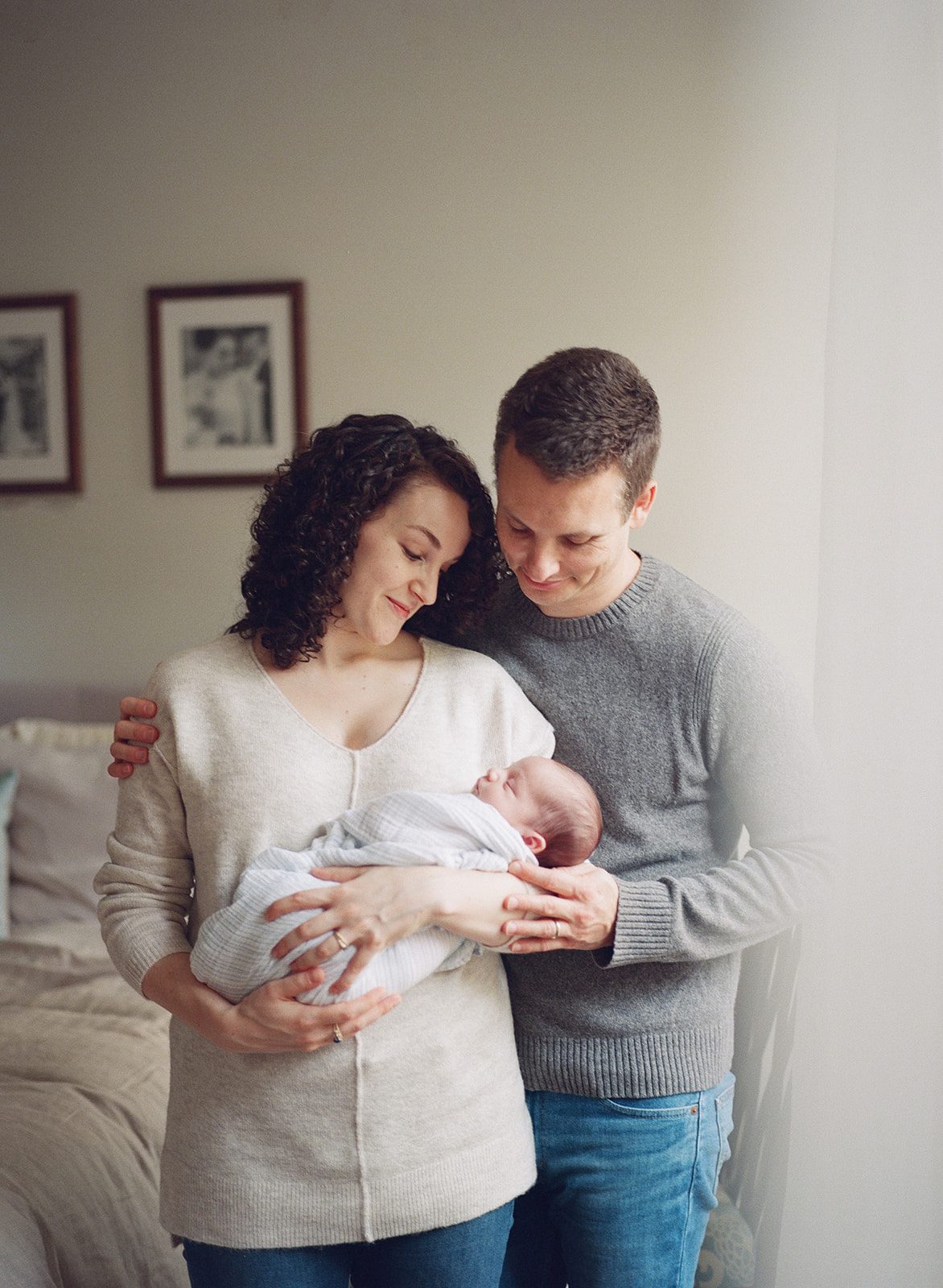 woman holds newborn and smiles at him while man wraps his arm around her