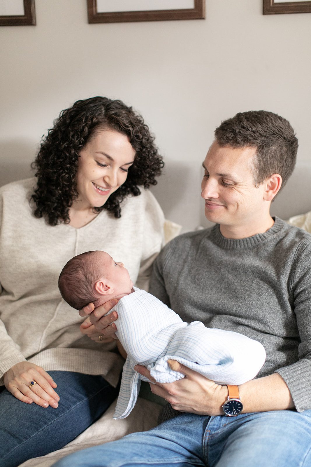 man and woman smile at newborn baby while sitting on couch