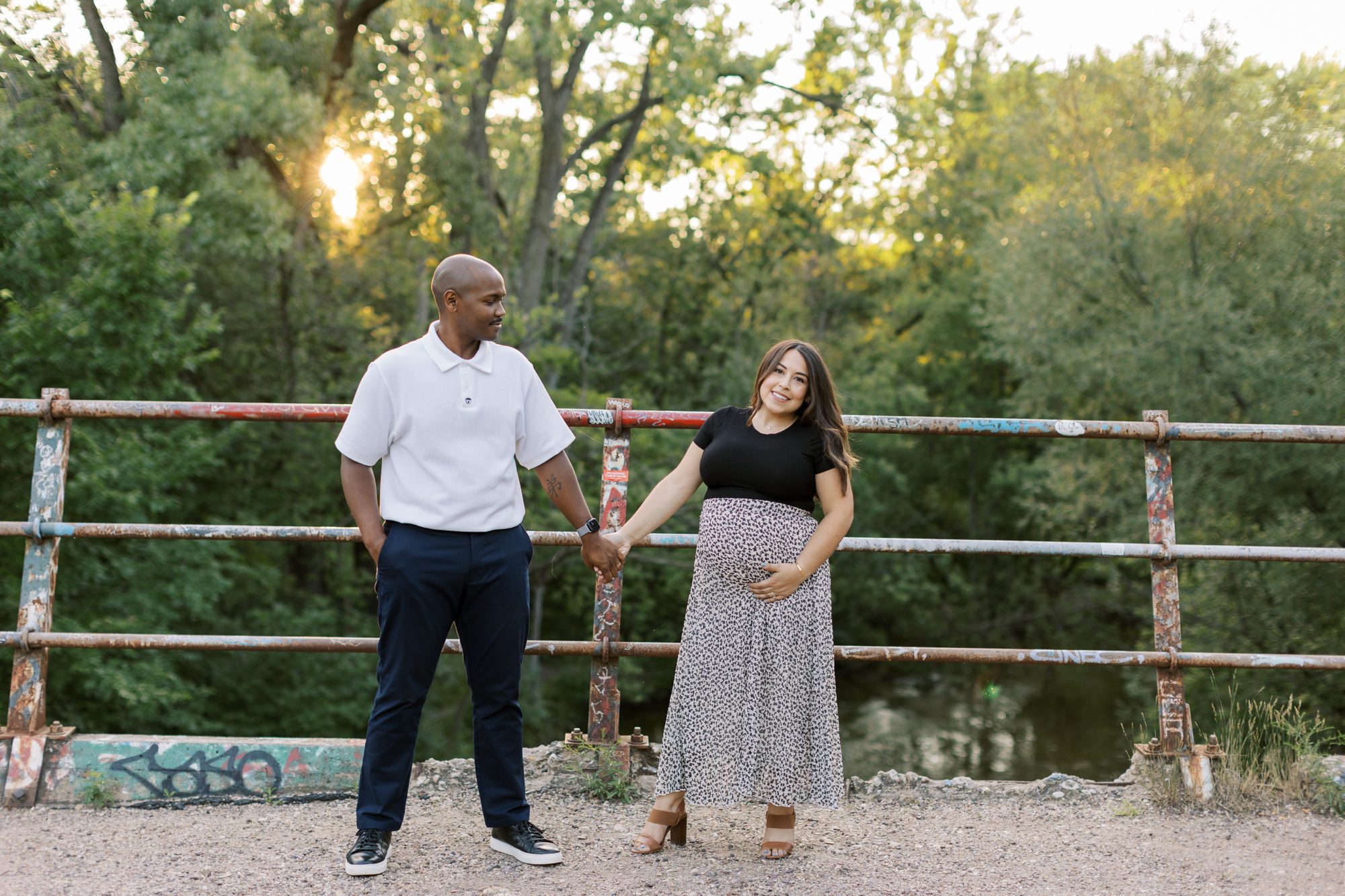 Man and woman hold hands during outdoor summer Chicago maternity photoshoot