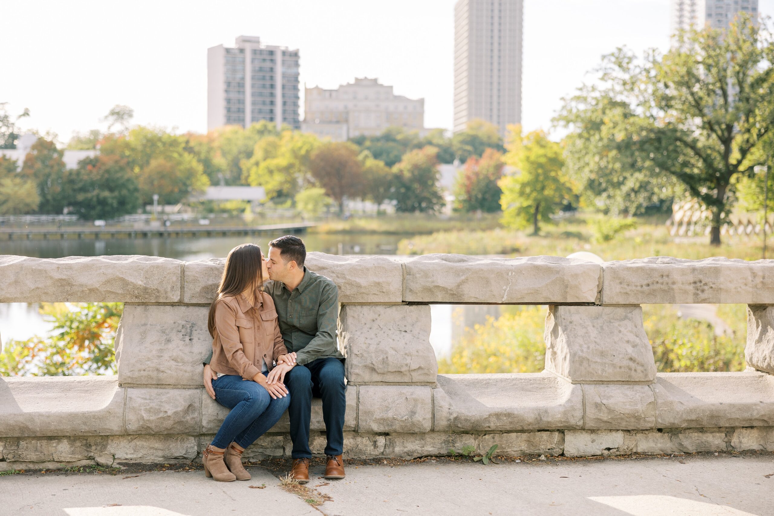Couple sits on bridge with Chicago skyline backdrop during engagement session